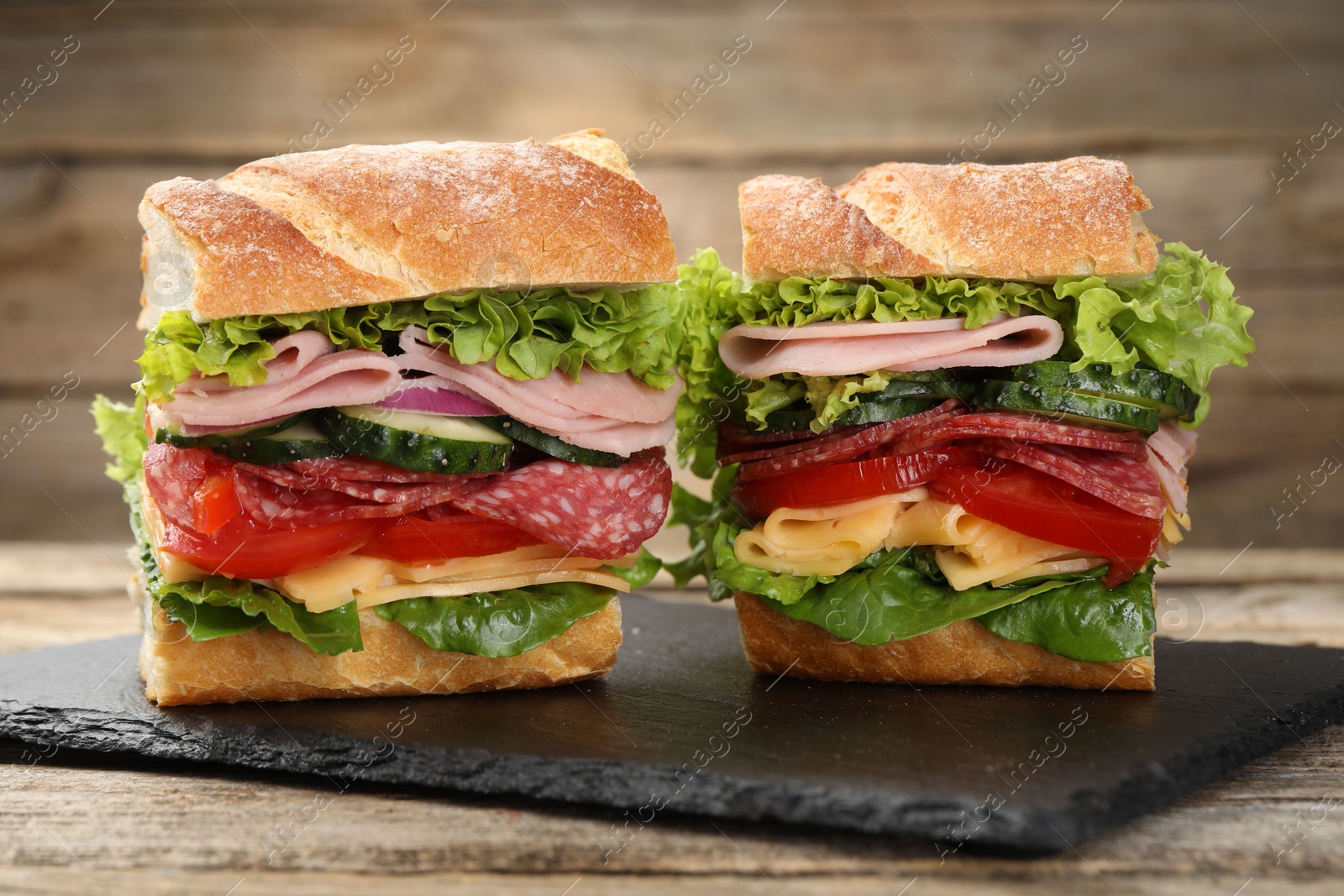 Photo of Tasty baguette sandwich with ham and vegetables on wooden table, closeup