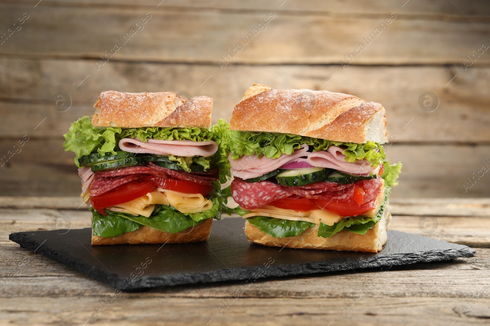 Tasty baguette sandwich with ham and vegetables on wooden table, closeup Photo of Tasty baguette sandwich with ham and vegetables on wooden table, closeup