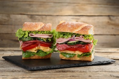 Photo of Tasty baguette sandwich with ham and vegetables on wooden table, closeup
