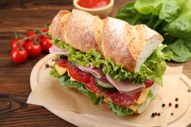 Photo of Tasty baguette sandwich with ham and vegetables on wooden table, closeup
