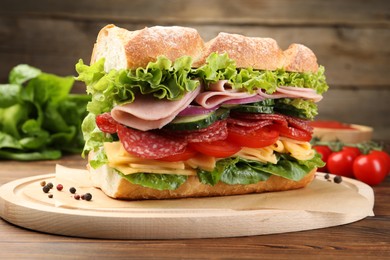 Photo of Tasty baguette sandwich with ham and vegetables on wooden table, closeup
