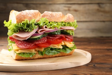 Photo of Tasty baguette sandwich with ham and vegetables on wooden table, closeup