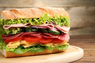Photo of Tasty baguette sandwich with ham and vegetables on wooden table, closeup