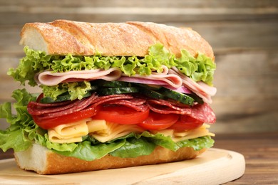 Photo of Tasty baguette sandwich with ham and vegetables on wooden table, closeup