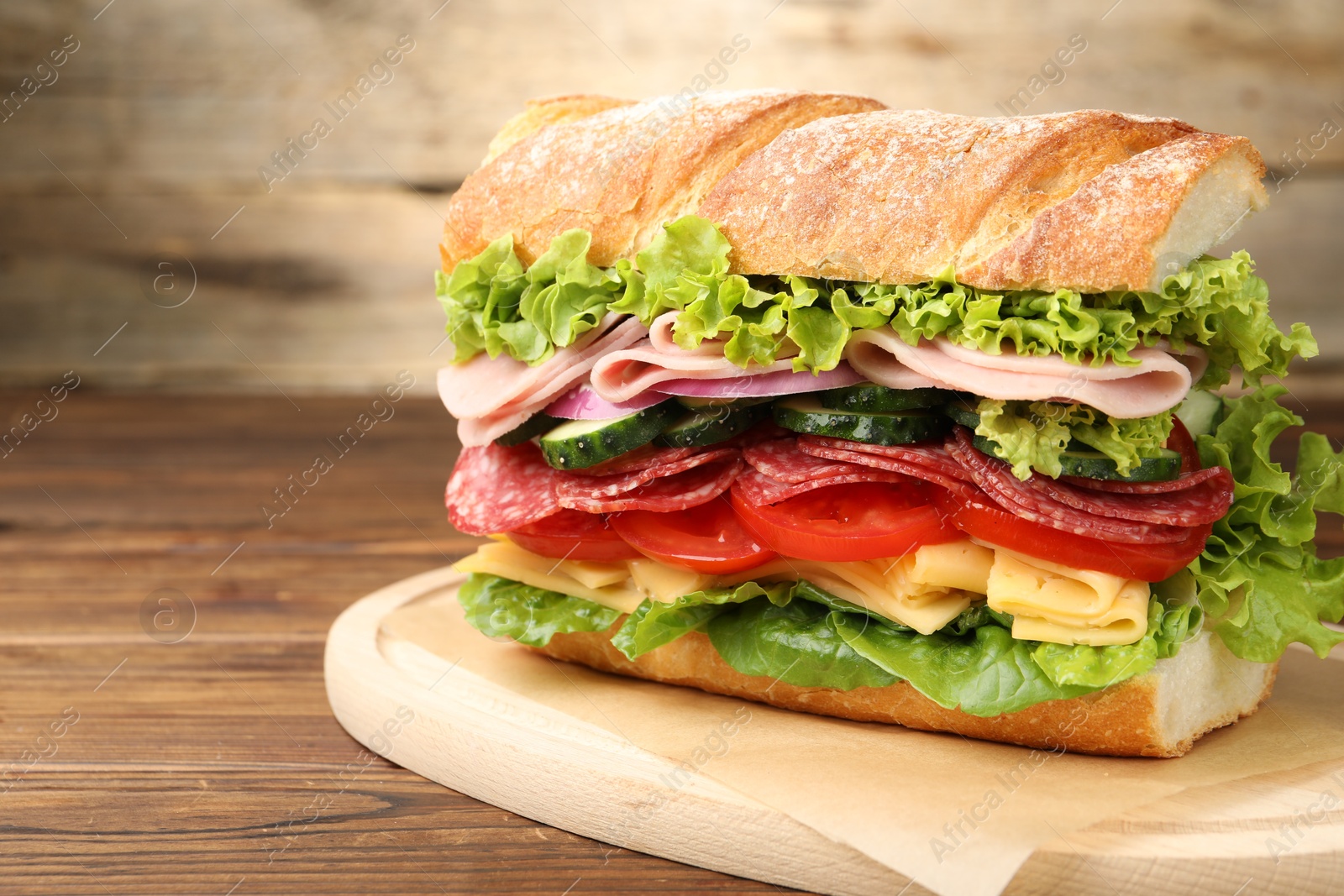 Tasty baguette sandwich with ham and vegetables on wooden table, closeup Photo of Tasty baguette sandwich with ham and vegetables on wooden table, closeup