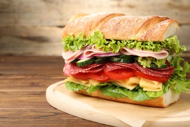 Photo of Tasty baguette sandwich with ham and vegetables on wooden table, closeup