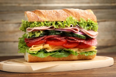 Photo of Tasty baguette sandwich with ham and vegetables on wooden table, closeup