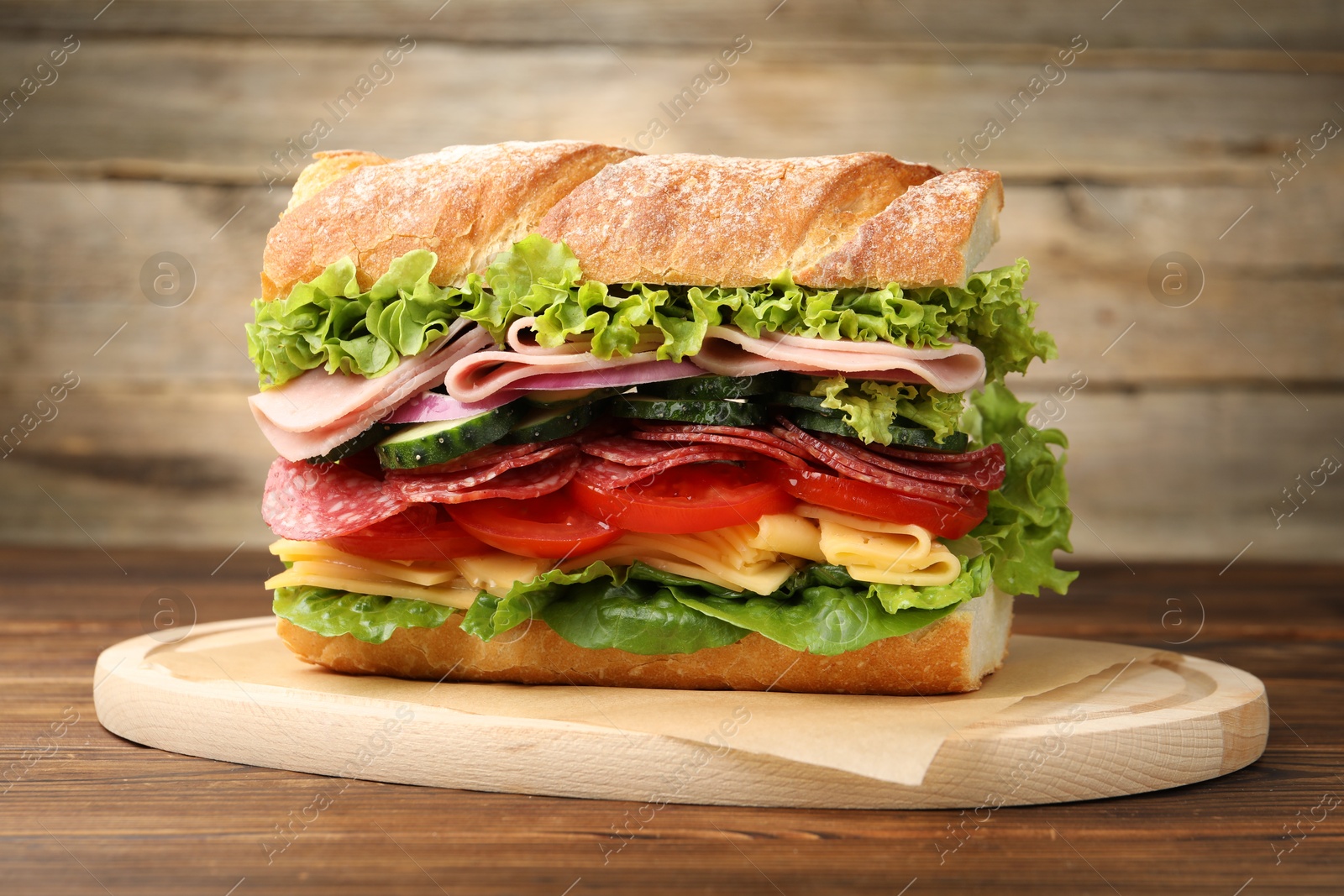 Tasty baguette sandwich with ham and vegetables on wooden table, closeup Photo of Tasty baguette sandwich with ham and vegetables on wooden table, closeup
