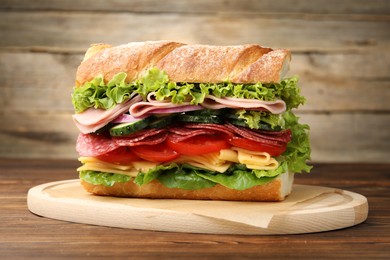 Photo of Tasty baguette sandwich with ham and vegetables on wooden table, closeup
