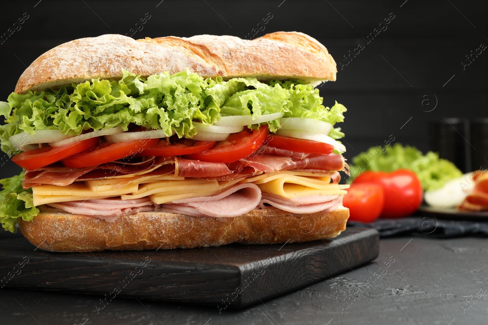 Tasty baguette sandwich with ham and vegetables on black table, closeup Photo of Tasty baguette sandwich with ham and vegetables on black table, closeup