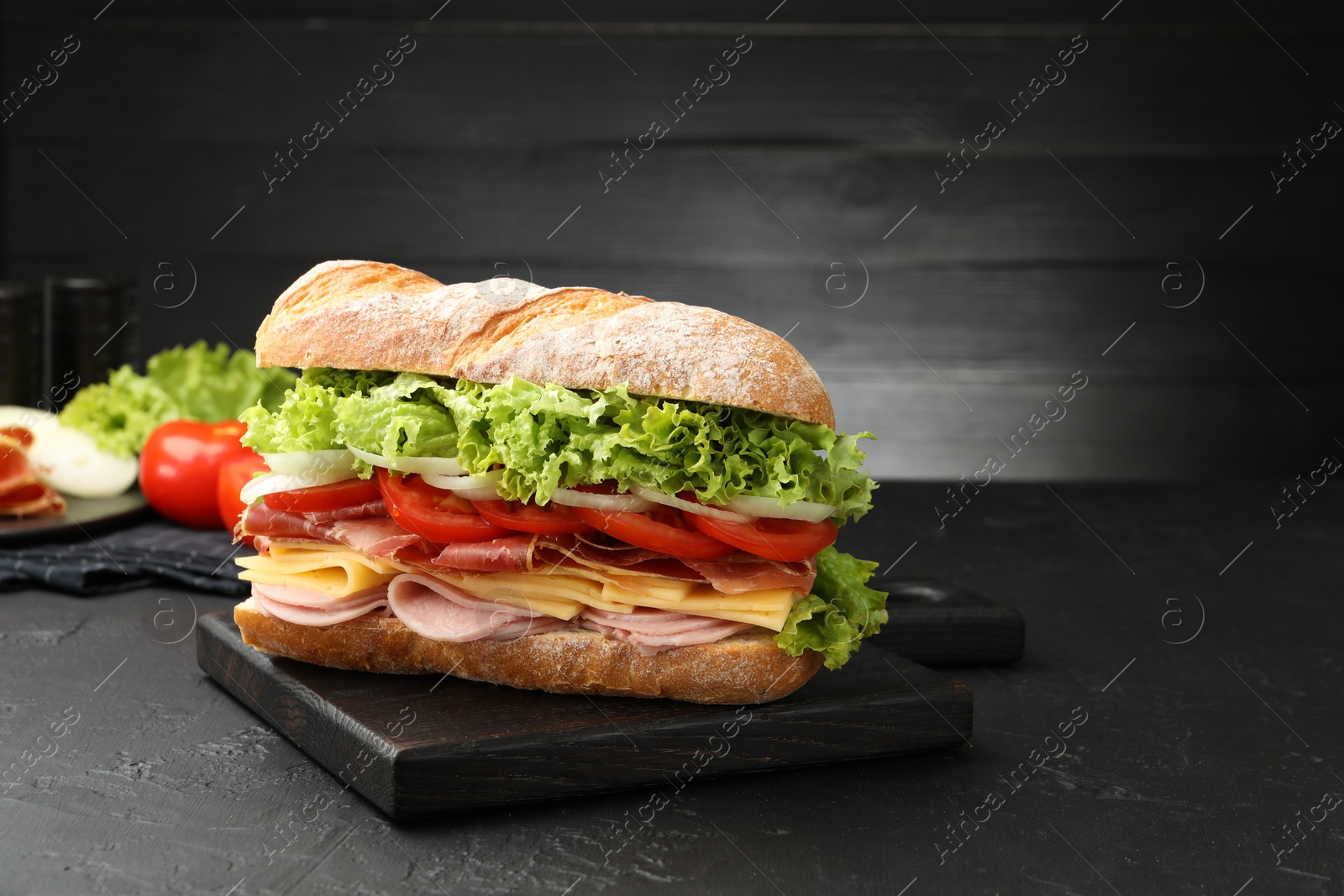 Tasty baguette sandwich with ham and vegetables on black table, closeup. Space for text Photo of Tasty baguette sandwich with ham and vegetables on black table, closeup. Space for text