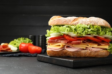 Photo of Tasty baguette sandwich with ham and vegetables on black table, closeup