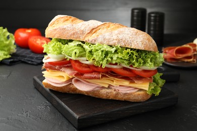 Photo of Tasty baguette sandwich with ham and vegetables on black table, closeup