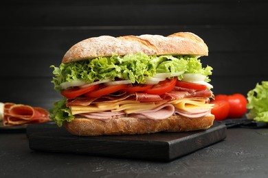 Photo of Tasty baguette sandwich with ham and vegetables on black table, closeup