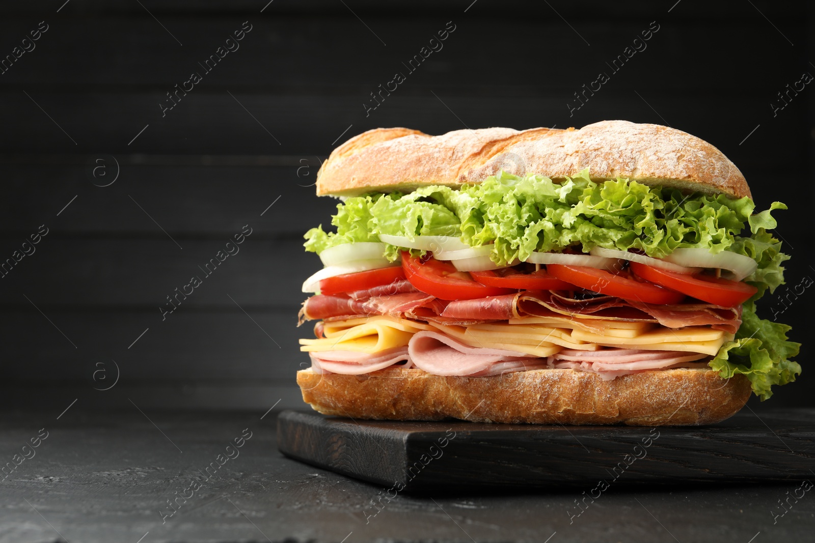 Tasty baguette sandwich with ham and vegetables on black table, closeup. Space for text Photo of Tasty baguette sandwich with ham and vegetables on black table, closeup. Space for text