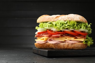 Photo of Tasty baguette sandwich with ham and vegetables on black table, closeup. Space for text