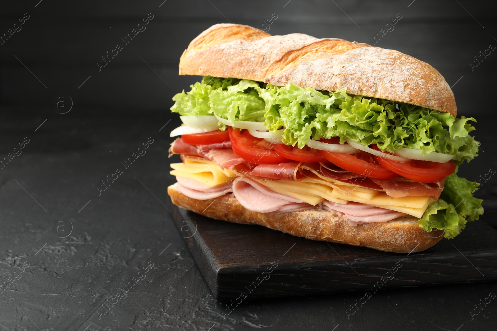 Tasty baguette sandwich with ham and vegetables on black table, closeup. Space for text Photo of Tasty baguette sandwich with ham and vegetables on black table, closeup. Space for text