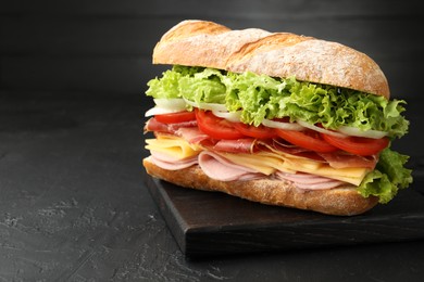 Photo of Tasty baguette sandwich with ham and vegetables on black table, closeup. Space for text