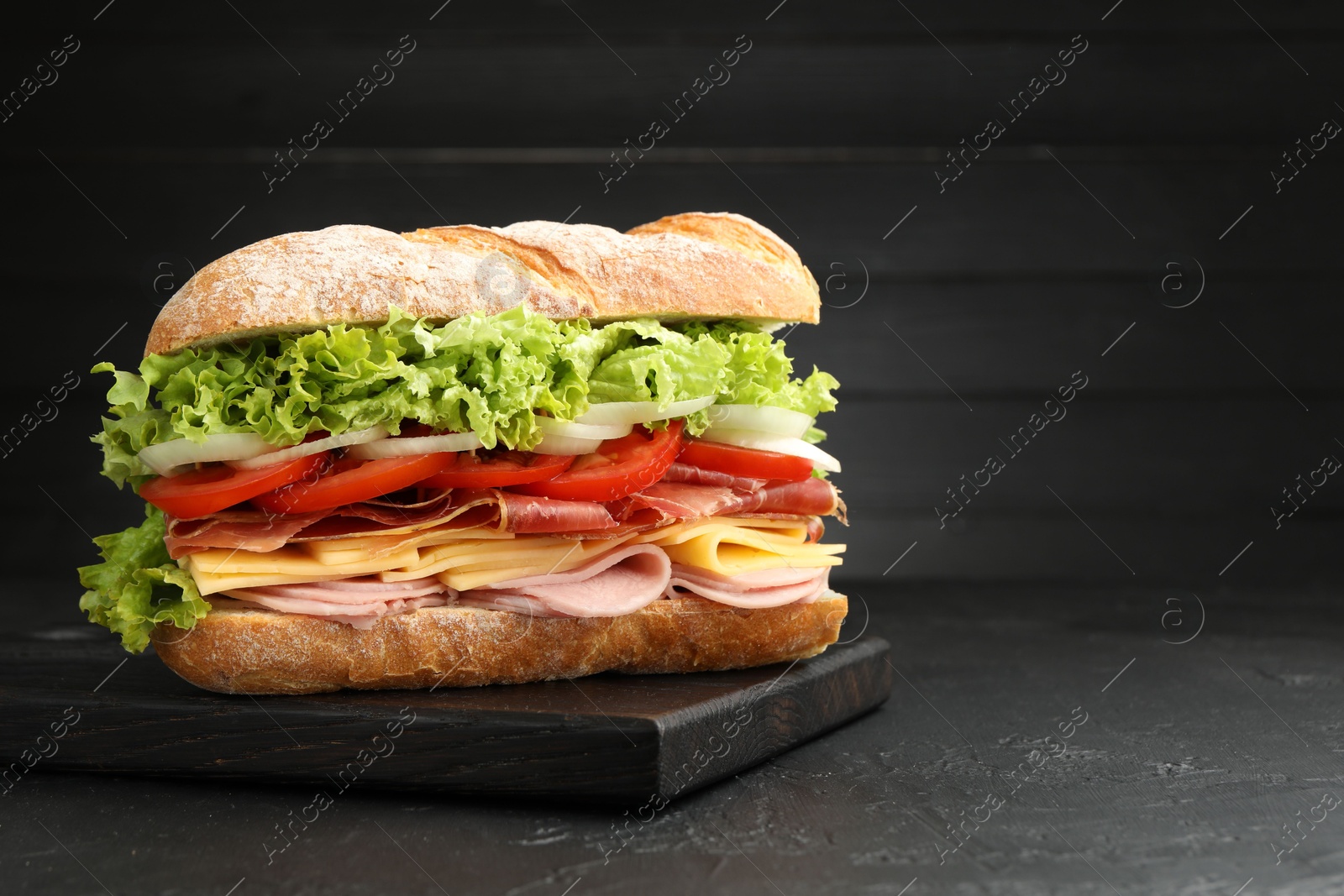 Tasty baguette sandwich with ham and vegetables on black table, closeup. Space for text Photo of Tasty baguette sandwich with ham and vegetables on black table, closeup. Space for text