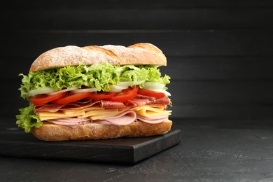 Photo of Tasty baguette sandwich with ham and vegetables on black table, closeup. Space for text