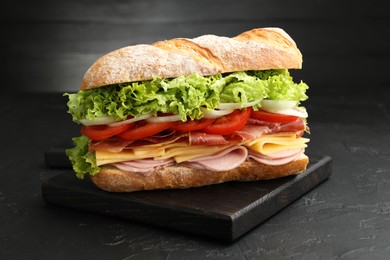 Photo of Tasty baguette sandwich with ham and vegetables on black table, closeup
