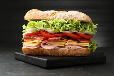 Photo of Tasty baguette sandwich with ham and vegetables on black table, closeup