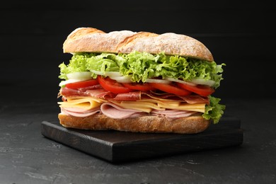 Photo of Tasty baguette sandwich with ham and vegetables on black table, closeup