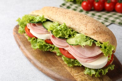 Photo of Tasty baguette sandwich with ham and vegetables on light grey table, closeup