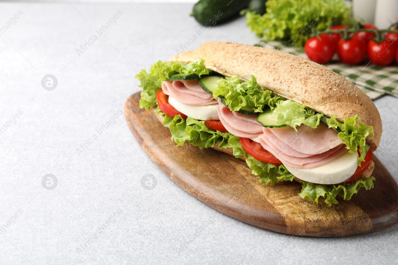 Tasty baguette sandwich with ham and vegetables on light grey table, closeup. Space for text Photo of Tasty baguette sandwich with ham and vegetables on light grey table, closeup. Space for text