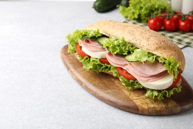 Photo of Tasty baguette sandwich with ham and vegetables on light grey table, closeup. Space for text