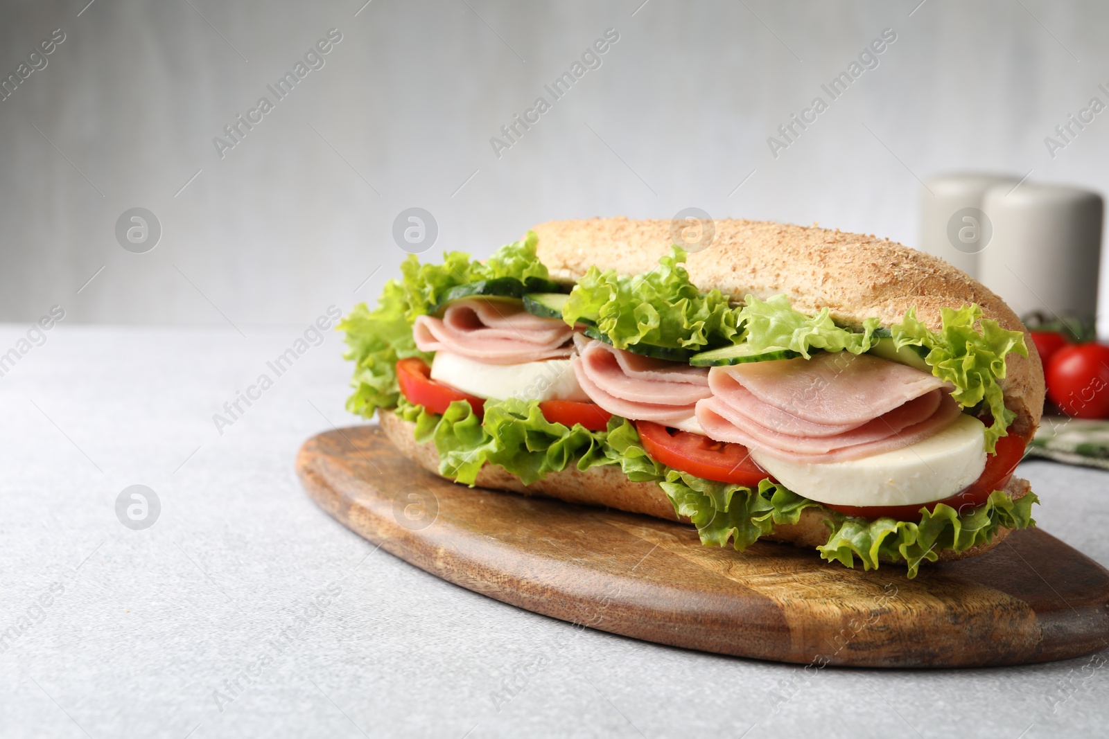 Tasty baguette sandwich with ham and vegetables on light grey table, closeup. Space for text Photo of Tasty baguette sandwich with ham and vegetables on light grey table, closeup. Space for text