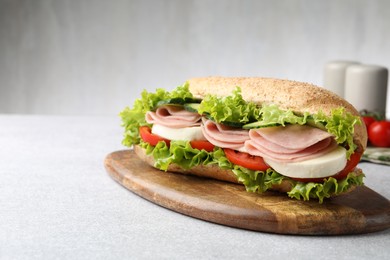 Photo of Tasty baguette sandwich with ham and vegetables on light grey table, closeup. Space for text