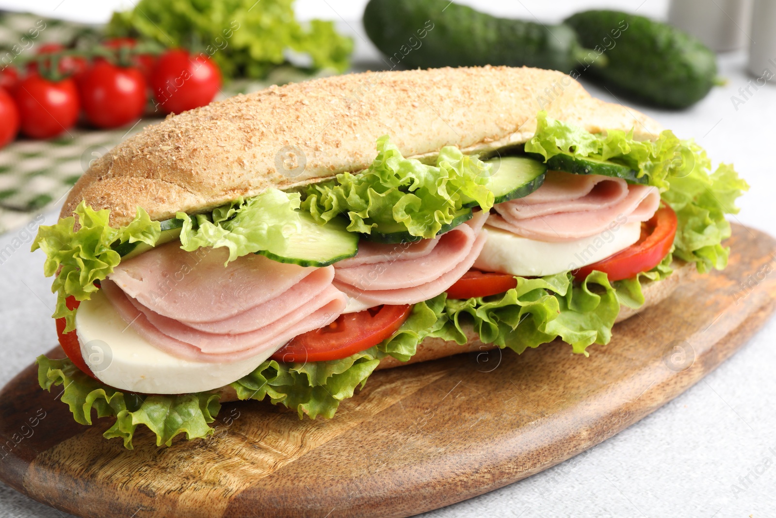 Tasty baguette sandwich with ham and vegetables on light grey table, closeup Photo of Tasty baguette sandwich with ham and vegetables on light grey table, closeup