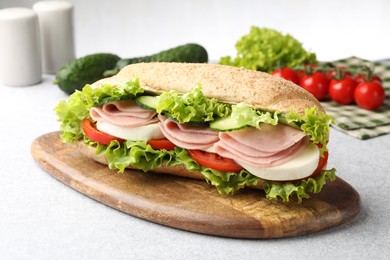 Photo of Tasty baguette sandwich with ham and vegetables on light grey table, closeup