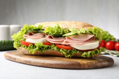 Photo of Tasty baguette sandwich with ham and vegetables on light grey table, closeup