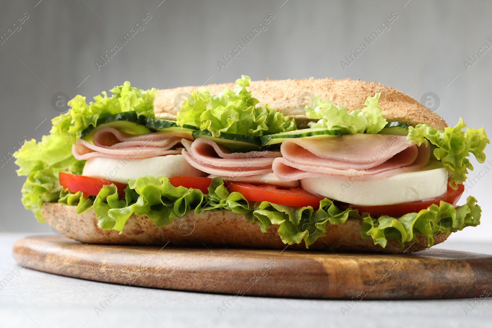 Tasty baguette sandwich with ham and vegetables on light grey table, closeup Photo of Tasty baguette sandwich with ham and vegetables on light grey table, closeup