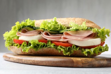 Photo of Tasty baguette sandwich with ham and vegetables on light grey table, closeup