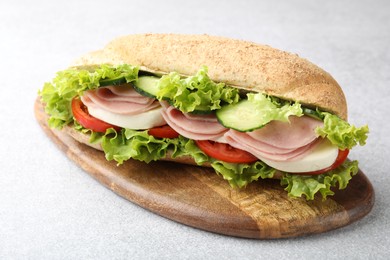 Photo of Tasty baguette sandwich with ham and vegetables on light grey table, closeup