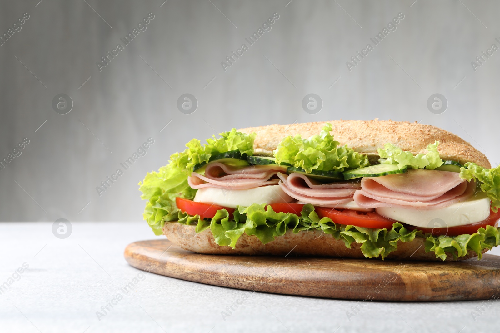 Tasty baguette sandwich with ham and vegetables on light grey table, closeup Photo of Tasty baguette sandwich with ham and vegetables on light grey table, closeup