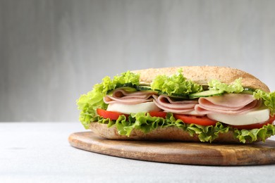Photo of Tasty baguette sandwich with ham and vegetables on light grey table, closeup