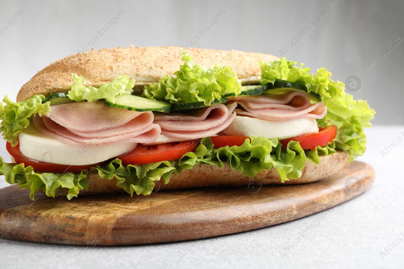 Tasty baguette sandwich with ham and vegetables on light grey table, closeup Photo of Tasty baguette sandwich with ham and vegetables on light grey table, closeup