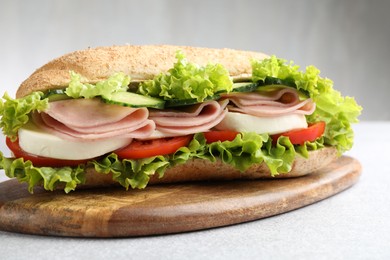 Photo of Tasty baguette sandwich with ham and vegetables on light grey table, closeup