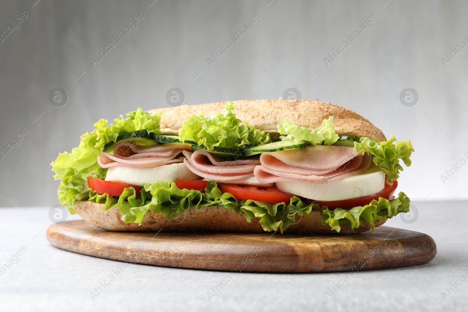 Tasty baguette sandwich with ham and vegetables on light grey table, closeup Photo of Tasty baguette sandwich with ham and vegetables on light grey table, closeup