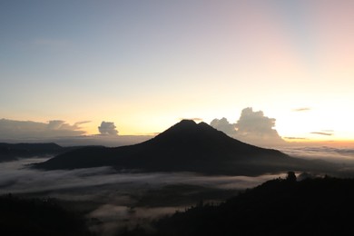 Photo of Picturesque view of mountains covered with fog on sunset