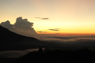 Photo of Picturesque view of mountains covered with fog on sunset