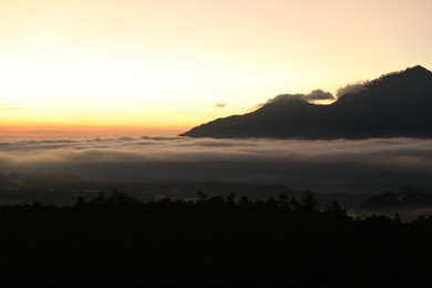 Photo of Picturesque view of mountains covered with fog on sunset