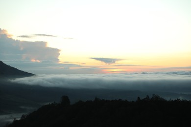 Photo of Picturesque view of mountains covered with fog on sunset