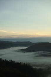 Photo of Picturesque view of mountains covered with fog on sunset