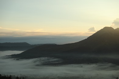 Photo of Picturesque view of mountains covered with fog on sunset