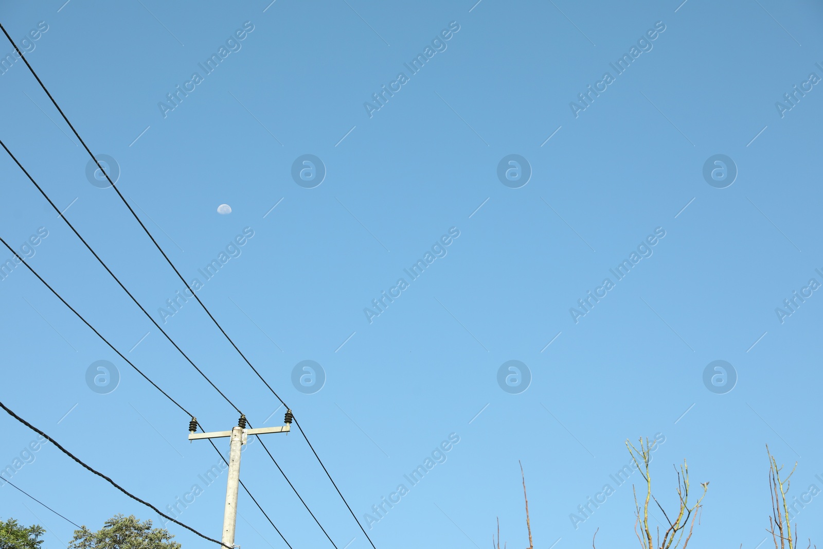Electricity pole and wires against blue sky with moon, low angle view Photo of Electricity pole and wires against blue sky with moon, low angle view